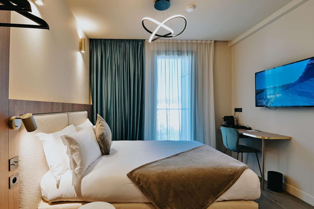 A modern hotel room with a large bed, a desk, and a TV on the wall.