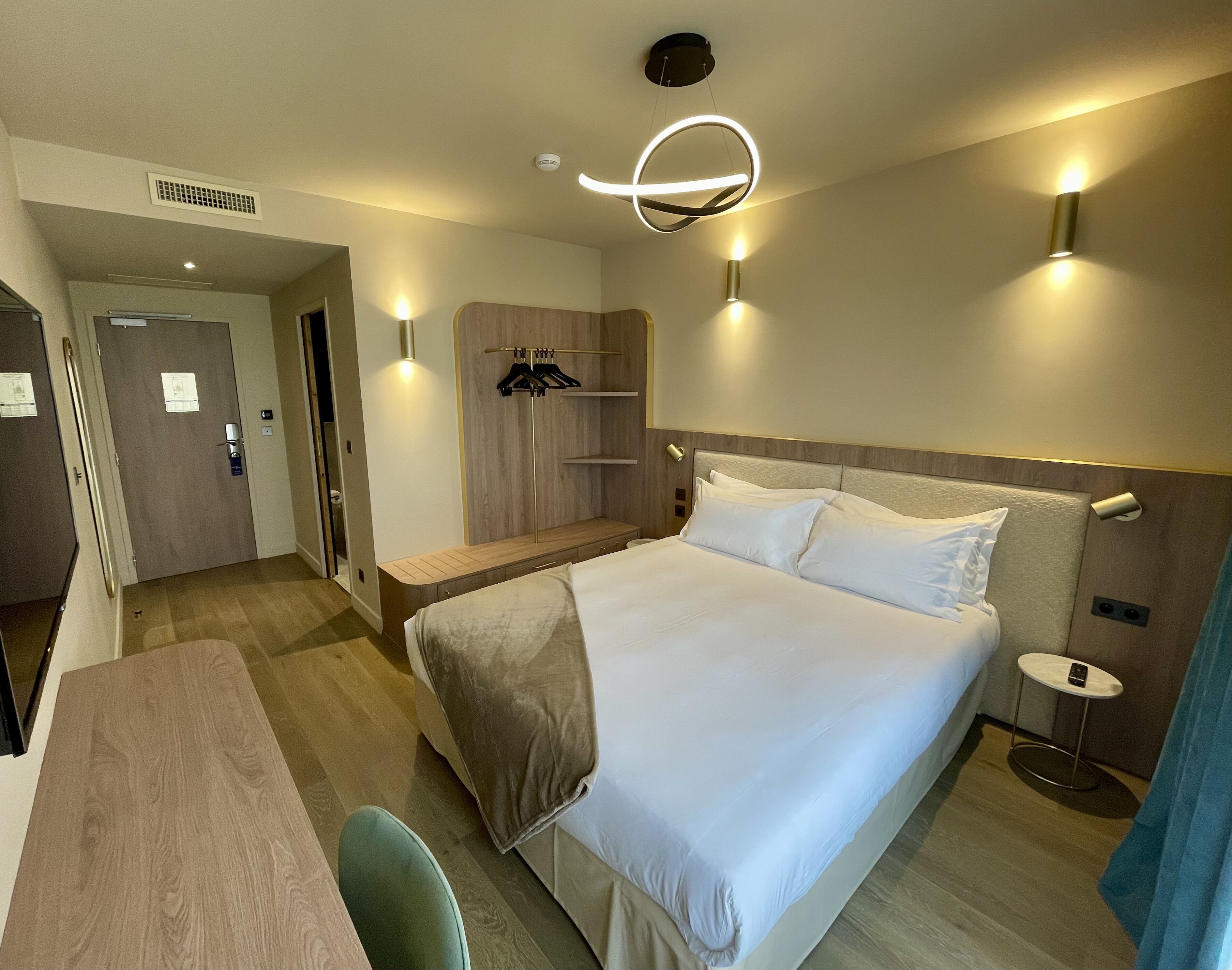 Une chambre d’hôtel comprenant un lit, une table de chevet et un coin salon avec un banc.