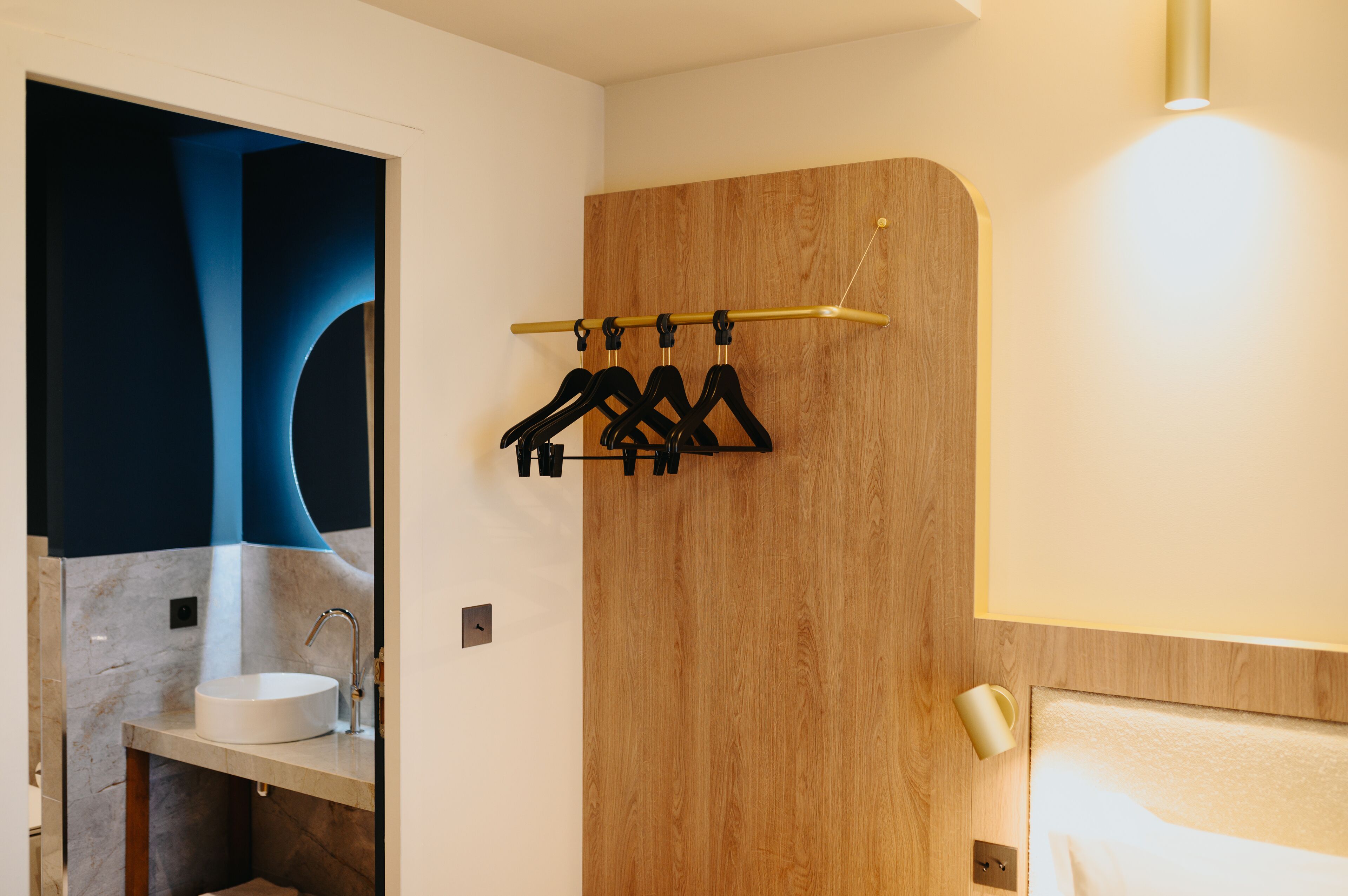 Une salle de bain moderne avec un lavabo en marbre, un mur recouvert de panneaux en bois et un porte-vêtements.