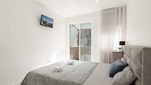 A bedroom with a bed, a nightstand, a window with curtains, and a wall-mounted picture. - Upscale Trendy Flats by HostWise (Porto)