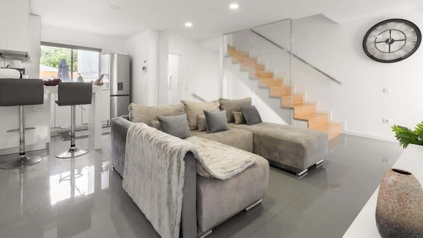 A modern living room with a sectional sofa, a glass staircase, and a kitchen area. - Upscale Trendy Flats by HostWise (Porto)