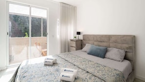 A bedroom with a bed, pillows, a nightstand, a lamp, and a view of the outdoors through a sliding door. - Upscale Trendy Flats by HostWise (Porto)