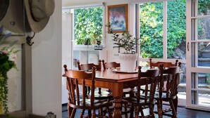 Un espace repas avec une table et des chaises en bois, entouré de grandes fenêtres donnant sur un paysage verdoyant.