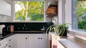 Une cuisine avec des meubles blancs, un plan de travail noir et une fenêtre donnant sur un arbre.