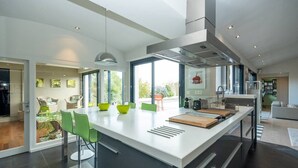 A modern kitchen with a large island, green chairs, and a view of the outdoors. - Calm'ré - Villa in a quiet area for family vacation (Sainte-Marie-de-Ré)