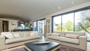 A modern living room with two sofas, a coffee table, and large windows offering a view of the outdoors. - Calm'ré - Villa in a quiet area for family vacation (Sainte-Marie-de-Ré)