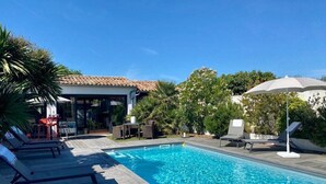 A swimming pool with lounge chairs, a covered area, and surrounding greenery. - Calm'ré - Villa in a quiet area for family vacation (Sainte-Marie-de-Ré)