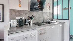 Une cuisine moderne équipée d’un lave-vaisselle, d’un grille-pain, d’une bouilloire et d ’un évier. Des ampoules sont suspendues au plafond et un tableau encadré orne le mur.