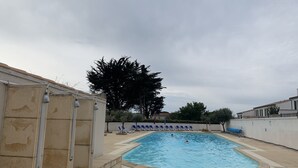 Une piscine avec des marches carrelées menant à l’eau, entourée d’un petit muret et bordée d’une rangée de chaises longues bleues.