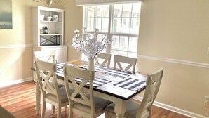 A dining area with a white table, chairs, and a vase of white flowers. There is a window with blinds, a chandelier, and a shelf with decorative items. - Bright centrally located 3 bed/2 bath with fenced private yard (Aiken)