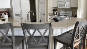 A kitchen with white cabinets, a microwave, a stove, and a sink. There are two wooden chairs with a cross-back design. - Bright centrally located 3 bed/2 bath with fenced private yard (Aiken)