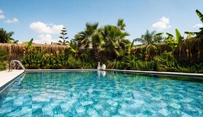 A clear blue pool surrounded by tropical vegetation and thatched structures. - Voger Alacati Silence (Cesme)