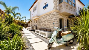 Un bâtiment à la façade en pierre, avec un scooter garé devant et des places assises à l’extérieur.