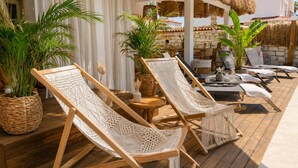 Une terrasse en bois avec des fauteuils de jardin en osier, un toit de chaume et des plantes en pot.