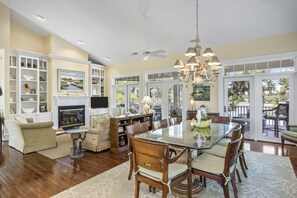 A spacious dining area with a large glass table surrounded by wooden chairs, a fireplace, and a view of the outdoors through large windows.