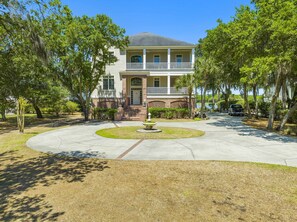 A two-story house with a front porch, a small garden with a fountain, and a driveway.