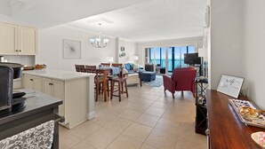 Eine moderne Küche mit Essbereich, ein Wohnzimmer mit einem roten Sessel und Blick ins Freie.