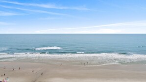 Ein Strand mit Menschen, die spazieren gehen und schwimmen, und einem klaren Himmel.