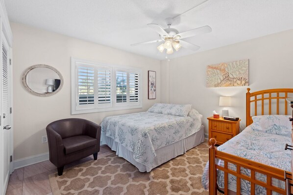 A bedroom with a bed, a chair, a nightstand, a ceiling fan, and a window with blinds. - ~ Beachfront Oasis ~ Oceanfront Condo in Arcadian One (Myrtle Beach)