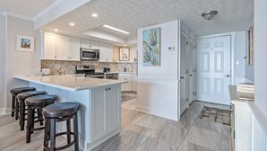 Una cocina moderna con armarios blancos, una isla grande con taburetes y electrodomésticos como microondas y refrigerador.