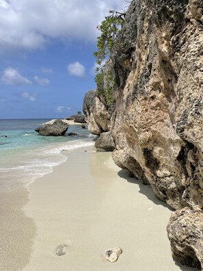 A beach with clear turquoise water, sandy shore, and rocky cliffs.