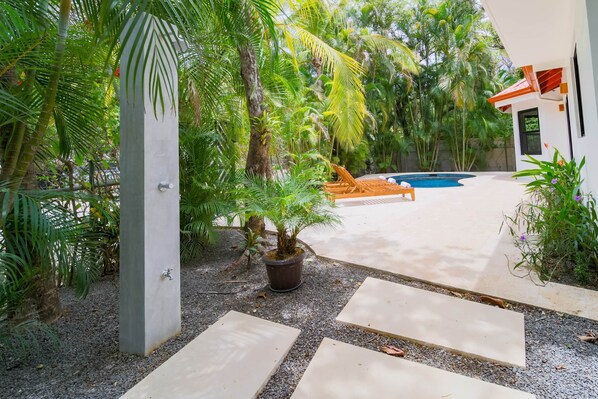 A modern outdoor pool area with a concrete pathway, lounge chairs, and lush tropical vegetation.