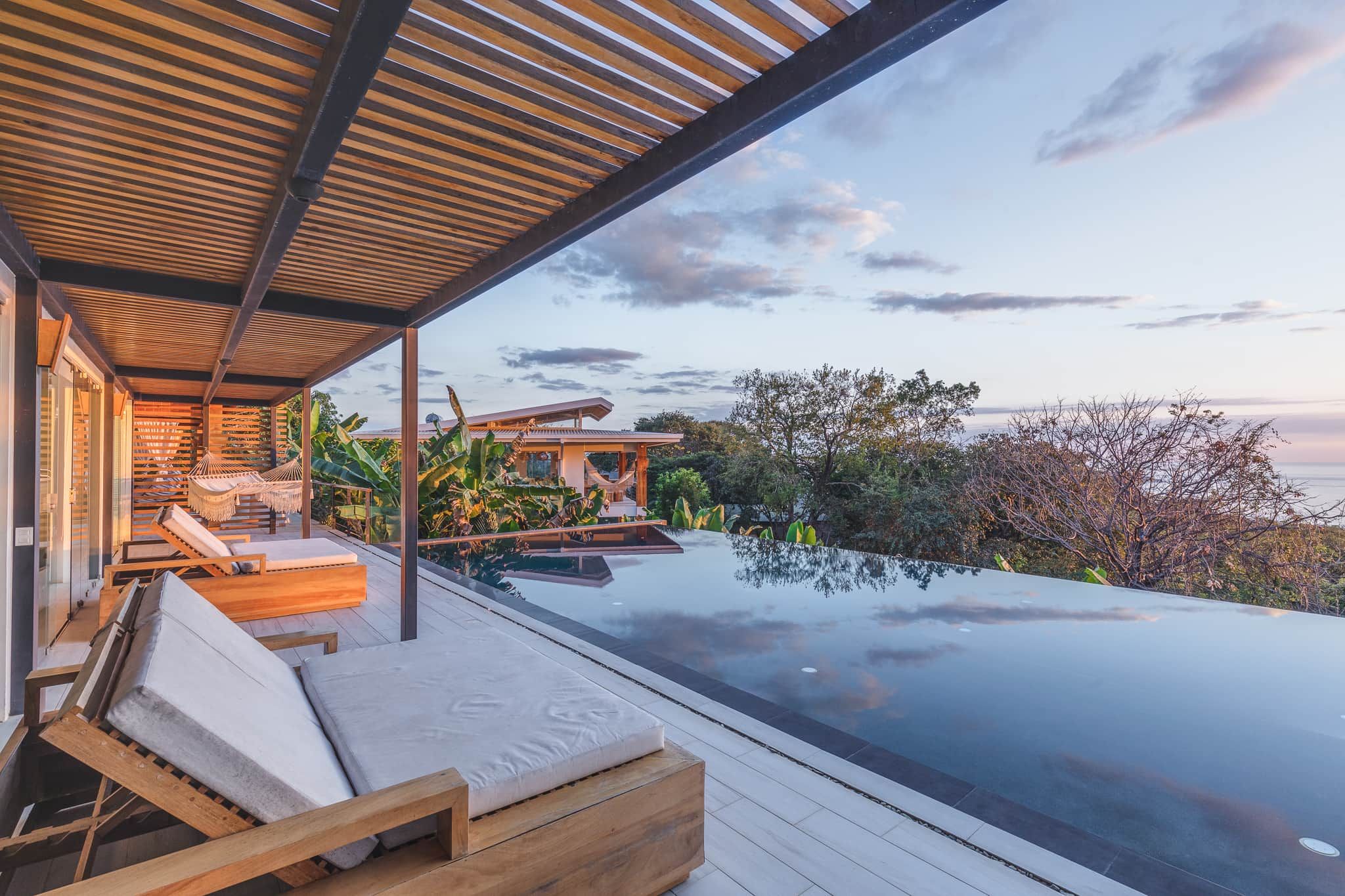A modern outdoor lounge area with a pool, wooden deck, and seating.