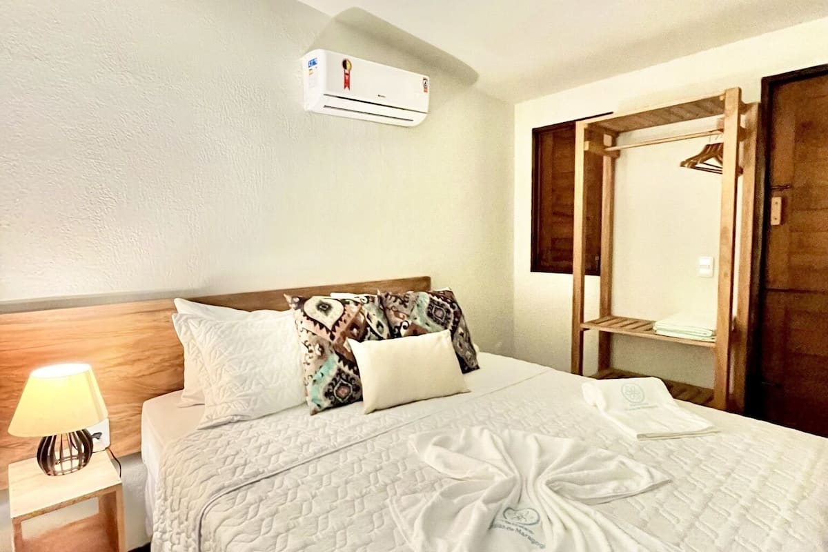 Een net opgemaakt bed met een decoratief kussen, een bedlampje en een houten hoofdbord.