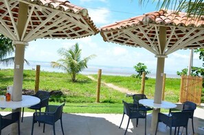Un área de estar al aire libre con mesas y sillas bajo una pérgola, con vista a un césped y una masa de agua.