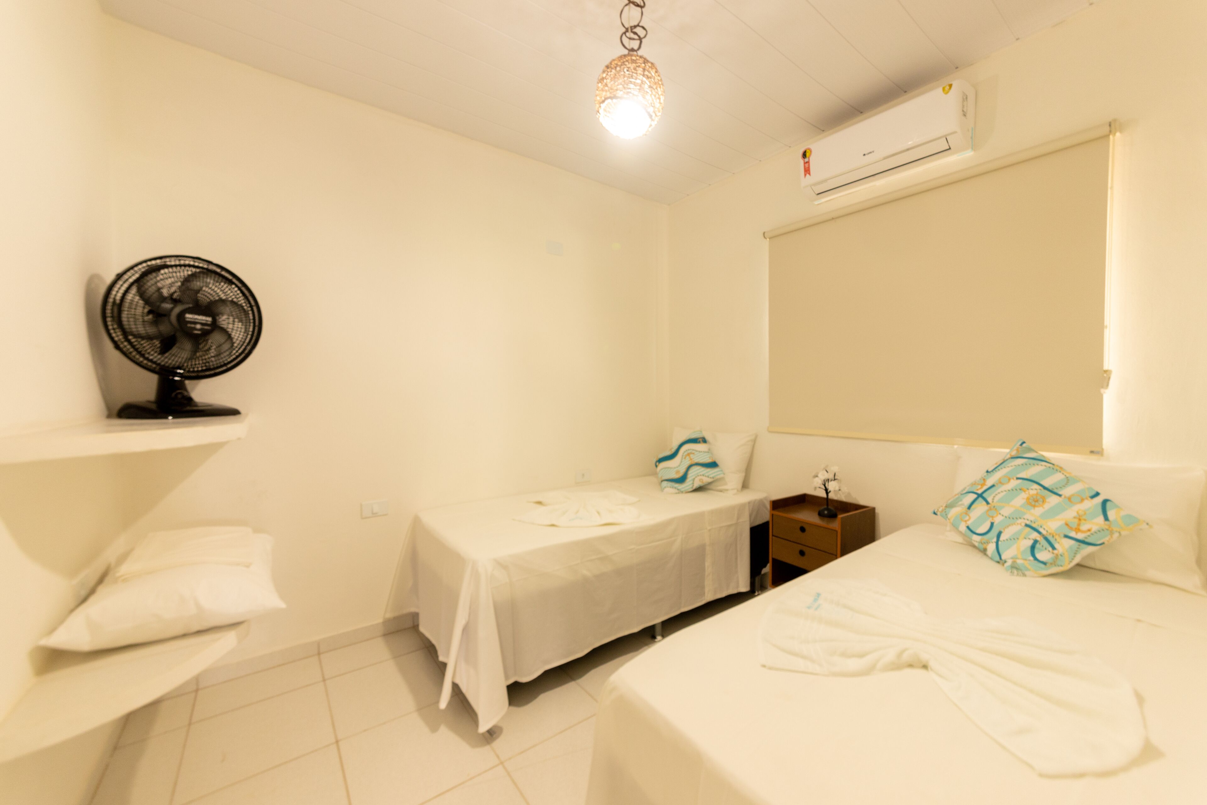 Een hotelkamer met een bed, nachtkastje, ventilator, raam.