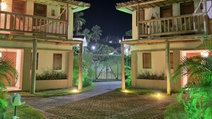 A nighttime view of a hotel entrance with a paved pathway leading to a gated entrance, surrounded by greenery and illuminated by artificial lighting. - Condominio Praias de Maragogi (Maragogi)