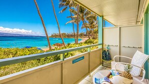 Ein Balkon mit Blick auf Strand und Meer, ein Stuhl, ein kleiner Tisch mit Schale und Ananas sowie ein Schild mit einer Nachricht.