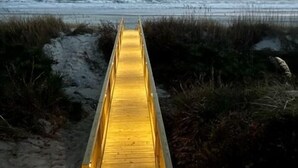 A wooden boardwalk leading to the beach, surrounded by sand and vegetation. - The Beachcomber- Stunning Oceanfront Home in PKS, NC (Pine Knoll Shores)