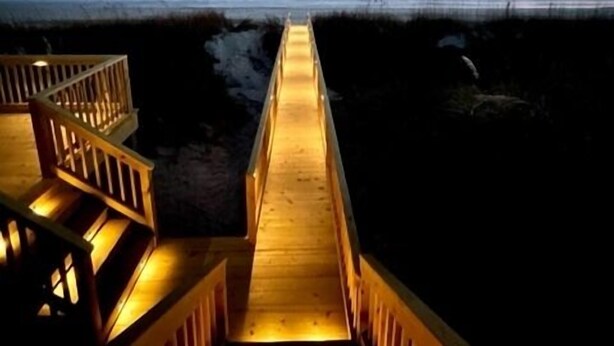 A wooden boardwalk leading to a beach with a staircase on the left. - The Beachcomber- Stunning Oceanfront Home in PKS, NC (Pine Knoll Shores)