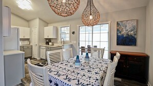 Una cocina moderna con armarios blancos, una mesa de comedor con mantel azul y blanco, y dos lámparas colgantes.