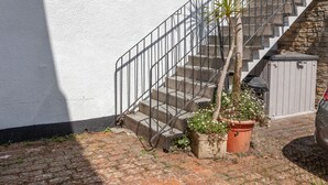 Un edificio residencial con fachada blanca, una escalera que conduce al segundo piso y plantas en macetas en el balcón.