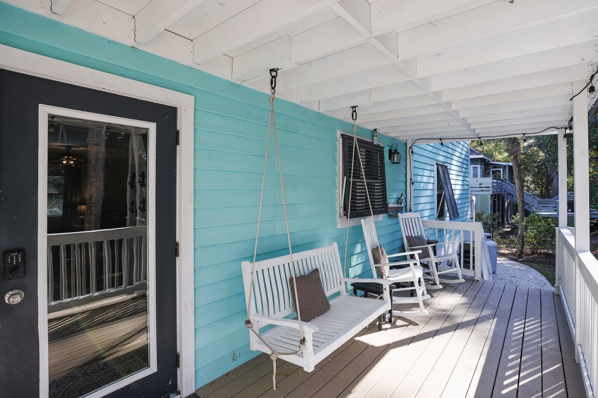 A porch with a white swing, two rocking chairs, and a door with a window.