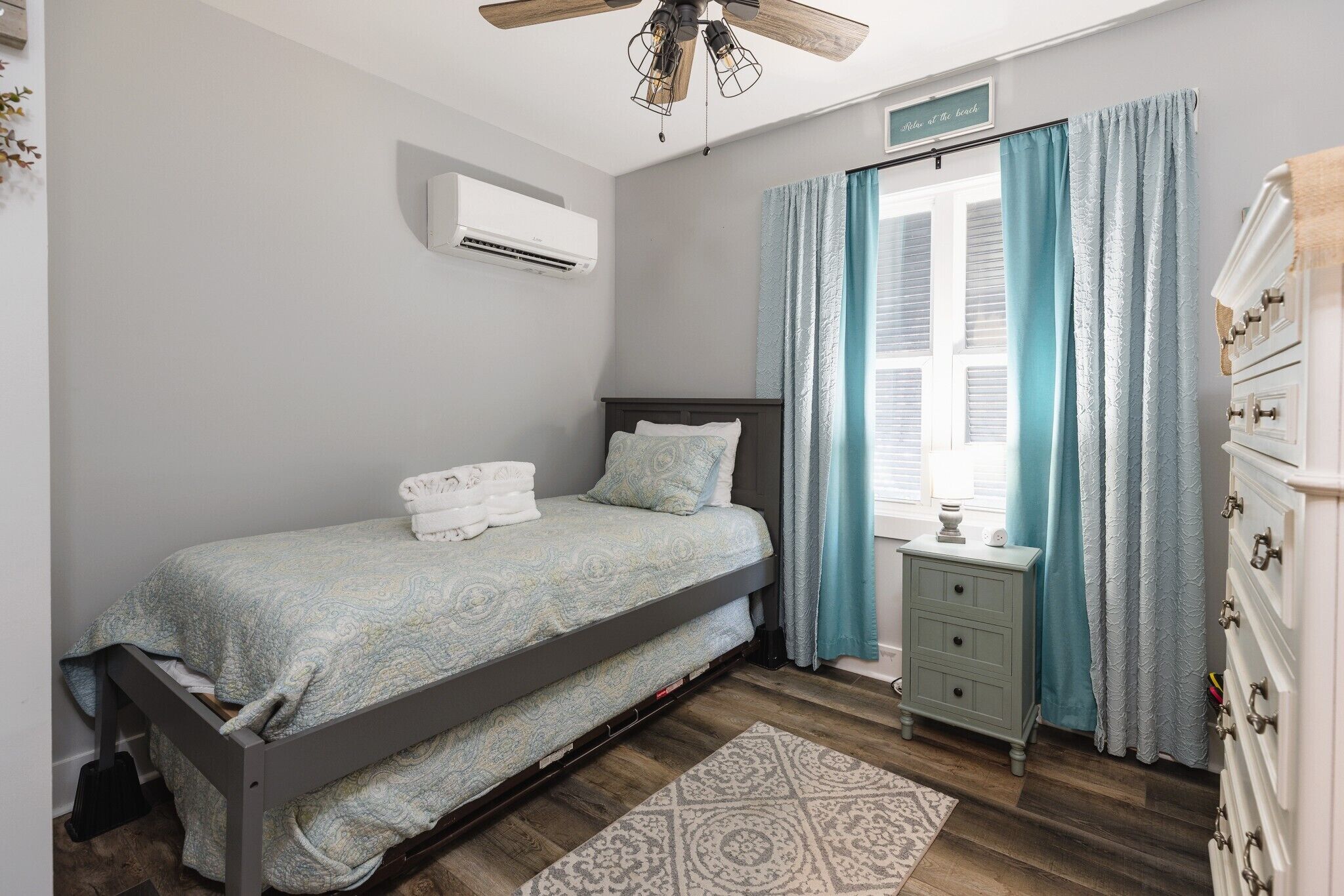 A bedroom with a bed, a nightstand, a dresser, a ceiling fan, and a window with curtains.