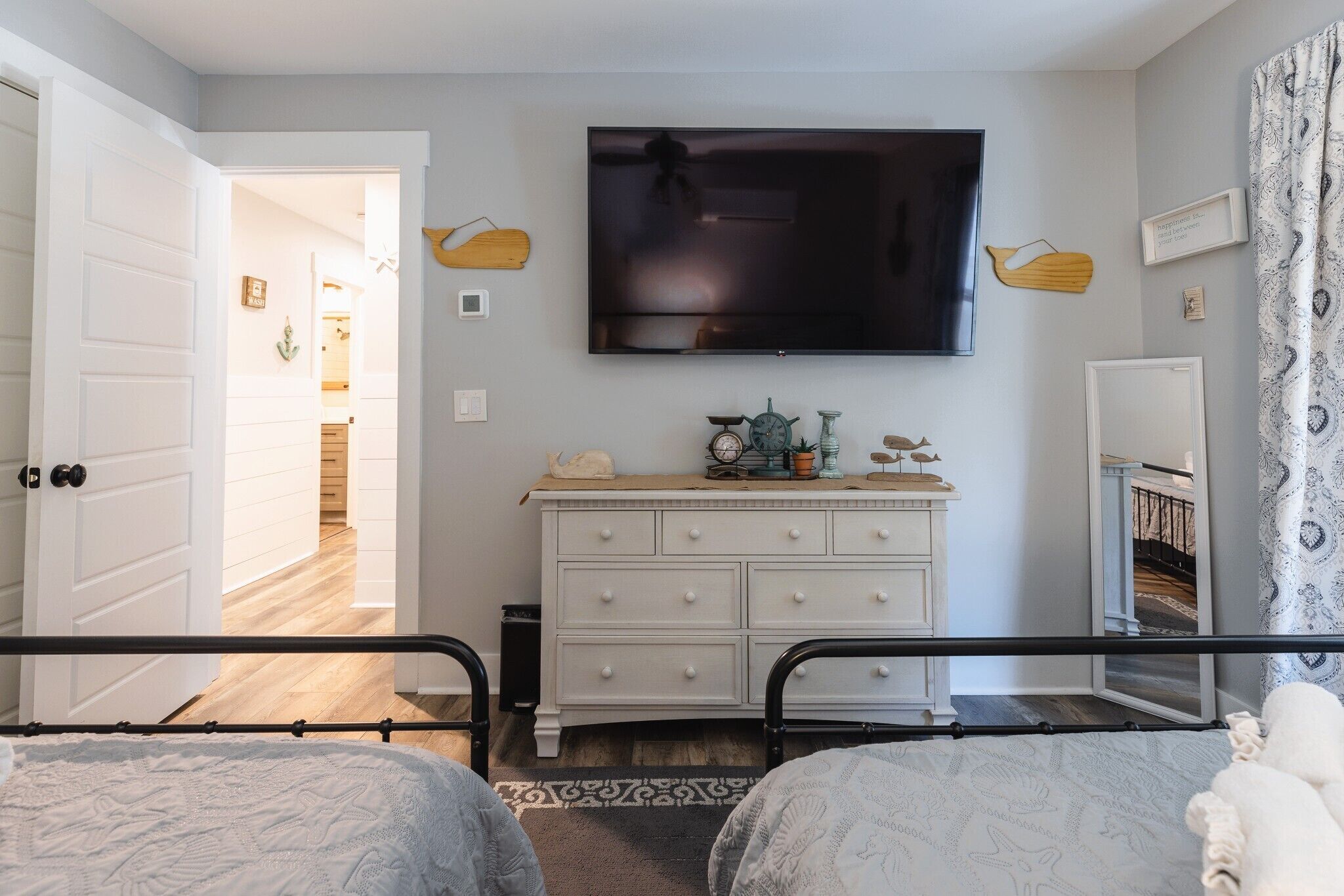 Une chambre à coucher comprenant un lit, une commode, un téléviseur et une porte donnant sur une autre pièce.