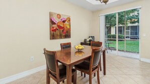 Un comedor con una mesa y sillas de madera, un cuadro en la pared, y vistas al patio trasero a través de un ventanal.