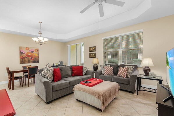 A living room with two grey sofas, a coffee table, a dining table, and a ceiling fan. - Beautiful Townhome close to HealthPark Medical Center (Fort Myers)