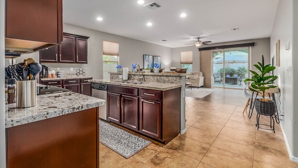 A modern kitchen with dark wood cabinets, granite countertops, and a large island. There is a dining area with a table and chairs, and a sliding glass door leading to a patio. - Gorgeous 3/2 Corner Lot with Firepit and Grassy Yard! (Gilbert)