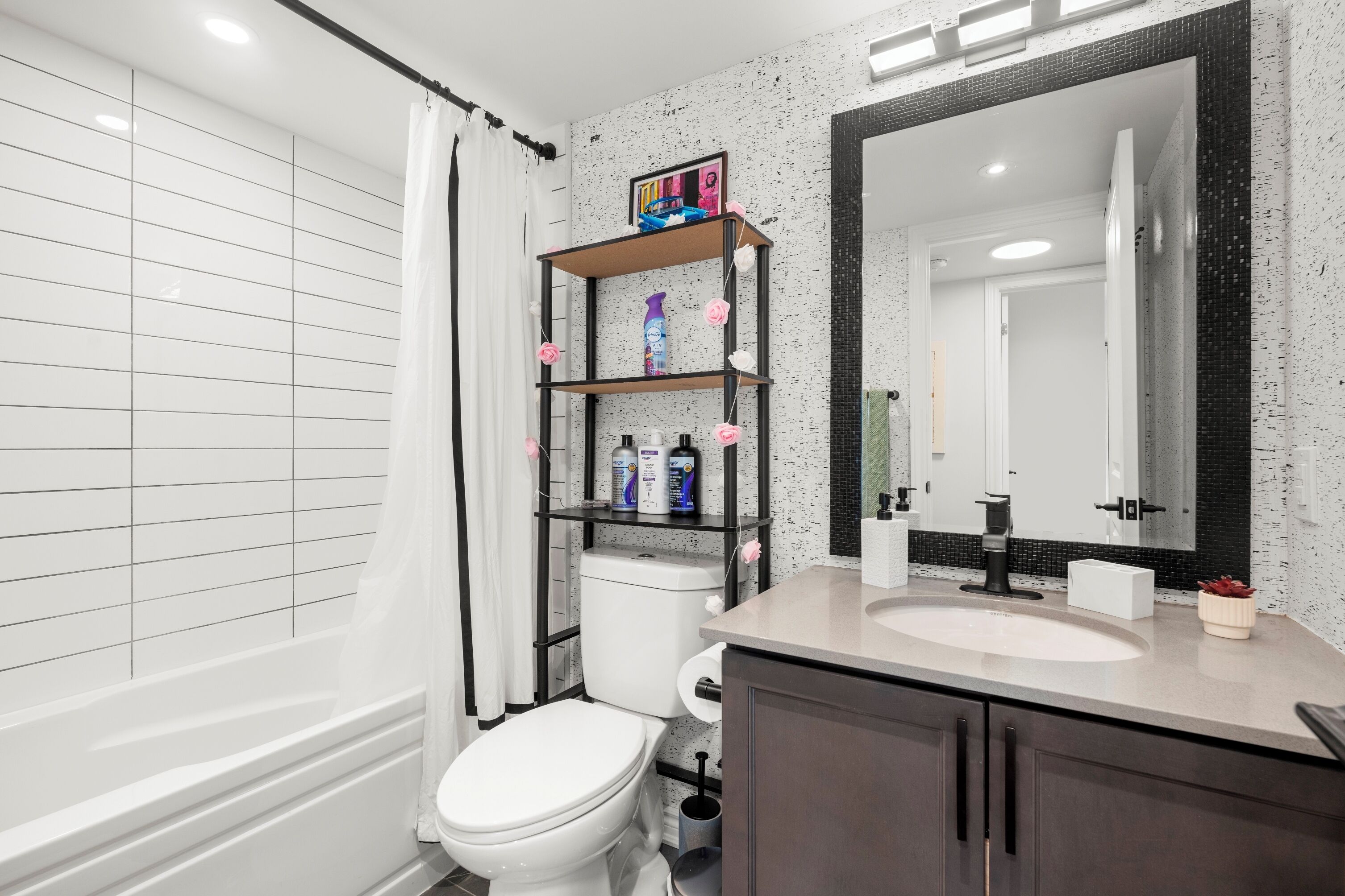 A bathroom with a white toilet, a shelf with toiletries, a large mirror, and a bathtub.