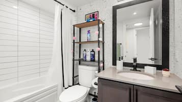 A bathroom with a white toilet, a shelf with toiletries, a large mirror, and a bathtub.
