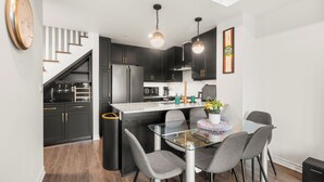 A modern kitchen with dark cabinets, a glass island, and a dining area with grey chairs. - Etobicoke Suites (Toronto)
