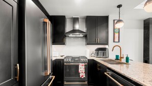 A modern kitchen with dark cabinetry, a stainless steel range, and a granite countertop. - Etobicoke Suites (Toronto)