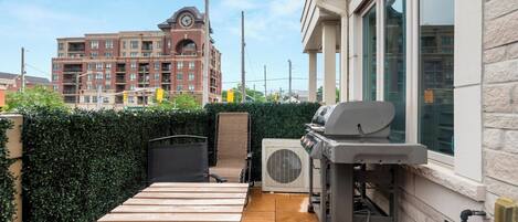 A patio with a table and chairs, a grill, and an air conditioning unit.