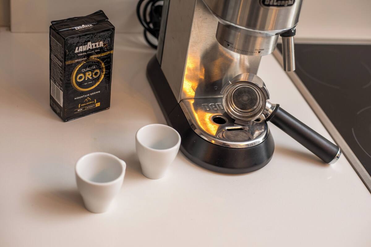En kaffemaskine med en kasse mærket "Lavazza" og to tomme kopper på en bordplade.