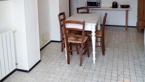 Un comedor con mesa y sillas blancas, una cocina con microondas y hervidor, y una escalera que lleva a un nivel superior.