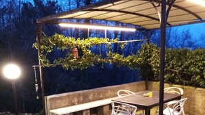 Un patio al aire libre con una mesa y sillas, un banco y una pérgola con plantas.